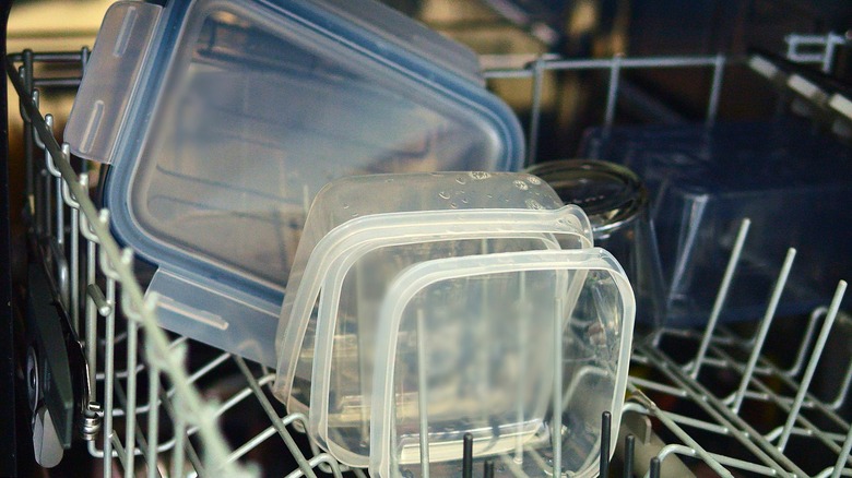 Plastic containers, lids, and short glasses on a top dishwasher rack