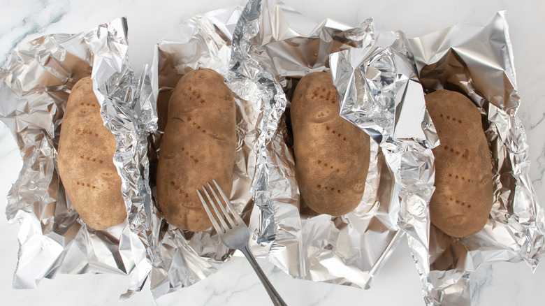 Four baking potatoes loosely wrapped in foil poked with a fork