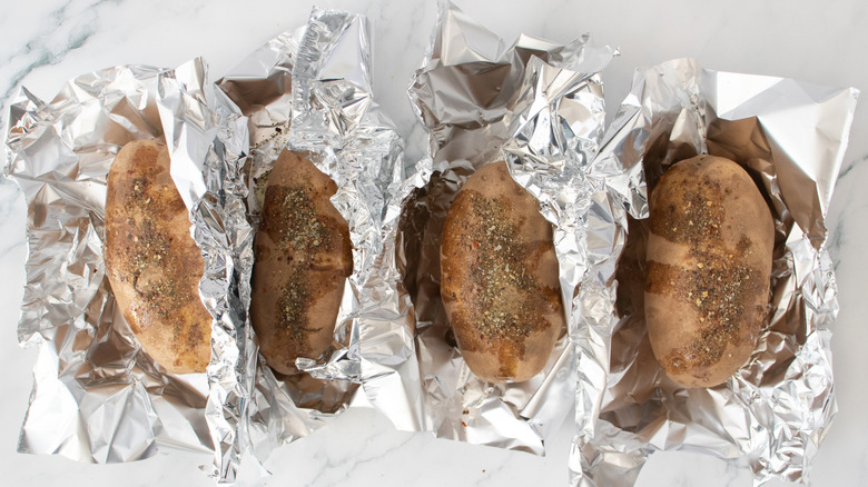 Four baking potatoes loosely wrapped in foil, seasoned and oiled