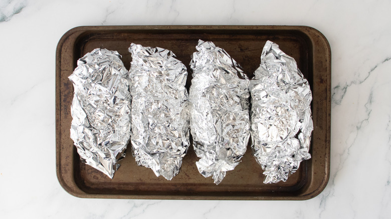 Foil-wrapped potatoes on a large baking sheet
