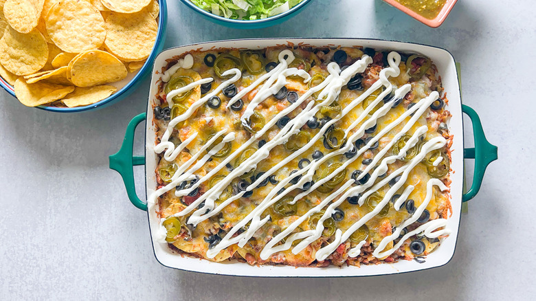 Tray of taco casserole next to bowl of chips