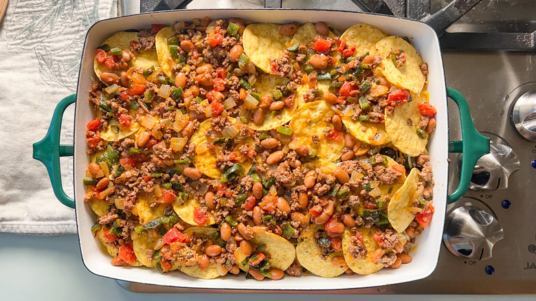 Ground beef, pinto beans, peppers, and tomatoes layered over tortilla chips in baking pan