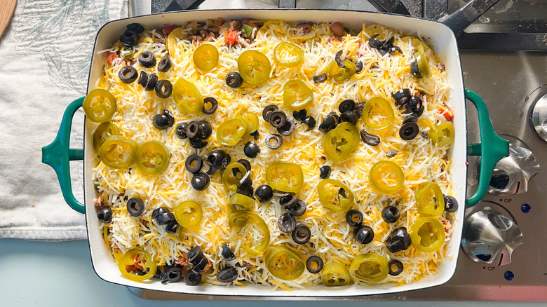 Pickled jalapeños, black olives, and shredded cheese on top of loaded beef taco casserole in baking dish