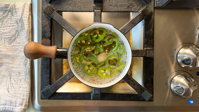 Sliced jalapeños cooking in brine in sauce pan on stovetop