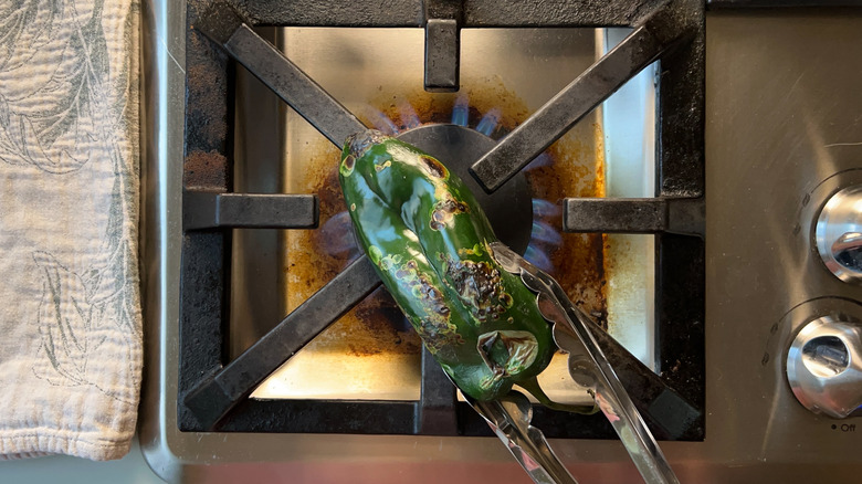Roasting poblano pepper over gas stove flame with tongs