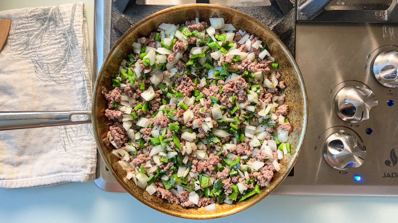 Ground beef, chopped onion, and chopped roasted poblano peppers in skillet on stovetop