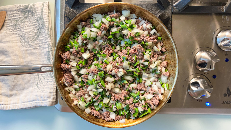 Ground beef, chopped onion, and chopped roasted poblano peppers in skillet on stovetop