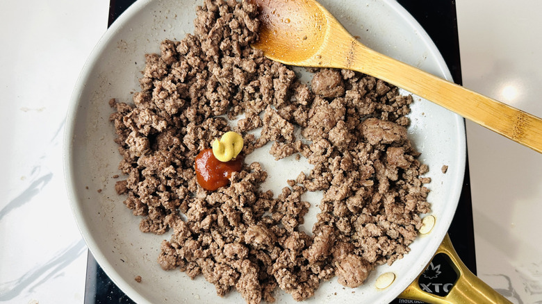 Cooked beef in skillet with ketchup and mustard