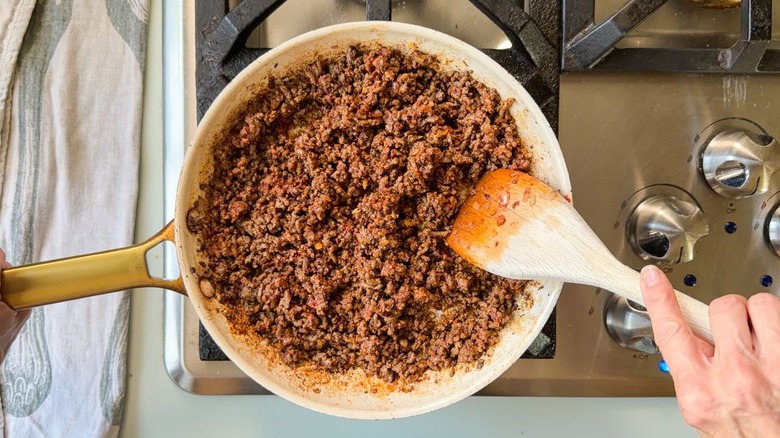 Stirring ground beef with ras el hanout in skillet on stovetop