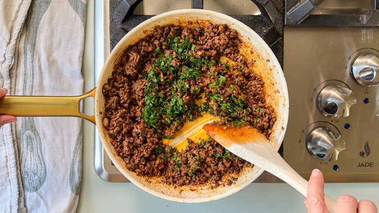 Stirring fresh chopped parsley into ras el hanout beef in skillet with wooden spoon