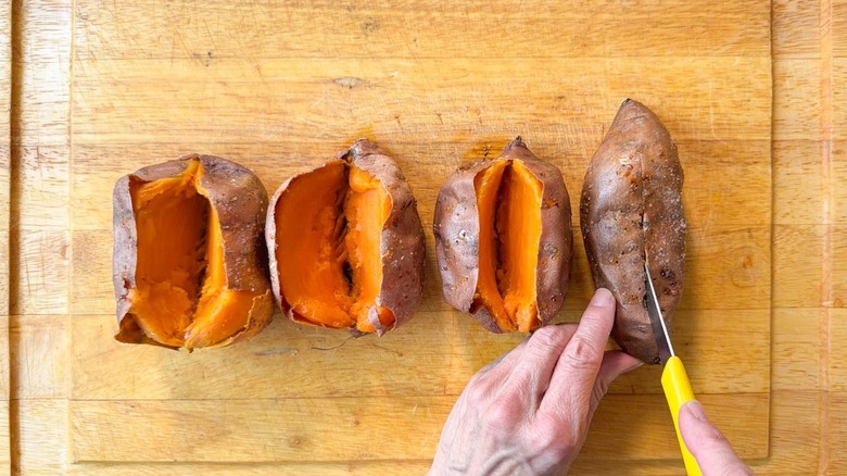 Cutting open baked sweet potatoes on cutting board