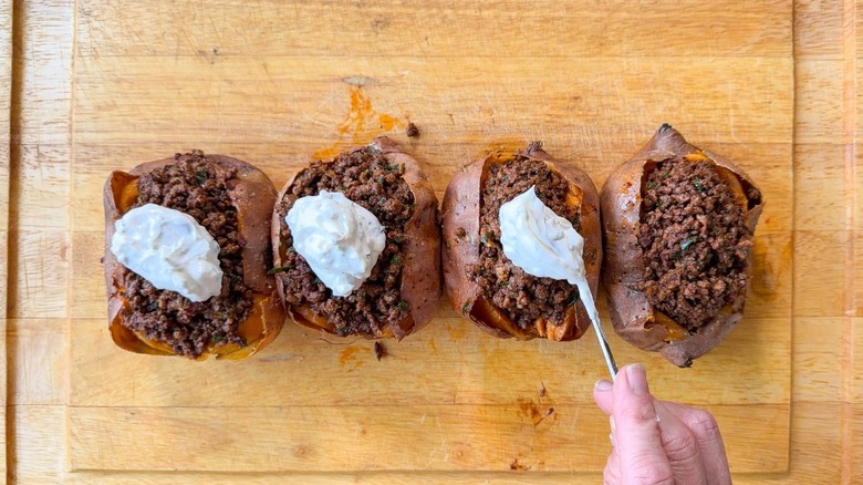 Topping loaded sweet potatoes with ras el hanout beef with lemon yogurt sauce on cutting board