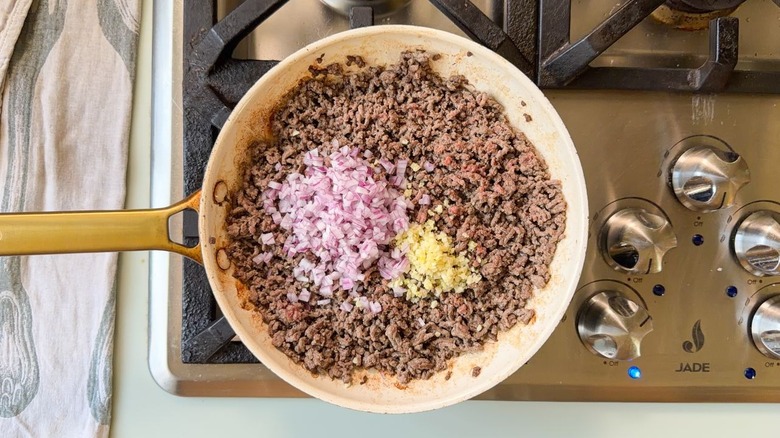 Browned ground beef, chopped red onion, and minced garlic in white skillet on stovetop