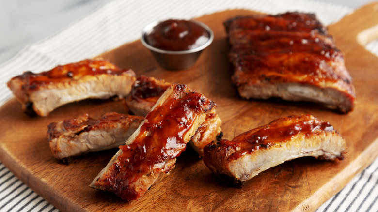 Baby back ribs on a wooden platter with a side of sauce