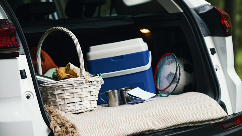 A cooler in the trunk along with other outdoorsy props, like a badminton racket, a picnic blanket, and a basket