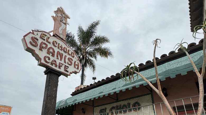 The neon sign of El Cholo Spanish Cafe with a palm tree behind it.