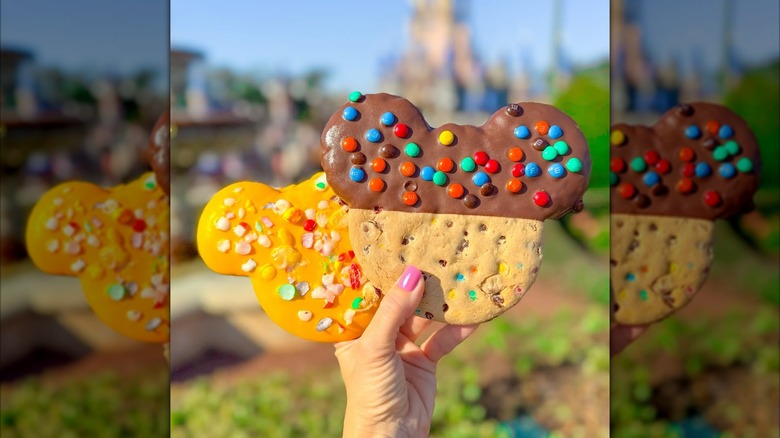 Hand holding Mickey Lemon & Strawberry Cookie with freeze-dried Skittles and Mickey Chocolate Chip Cookie made with Mini M&M's