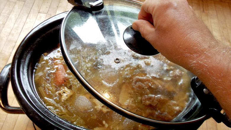 someone taking the lid off of a slow cooker