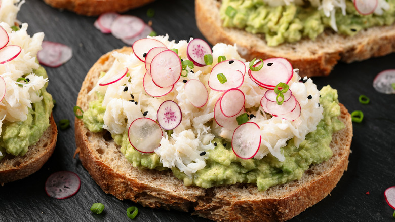 Crab toast featuring crab meat, sliced radishes, and smashed avocado