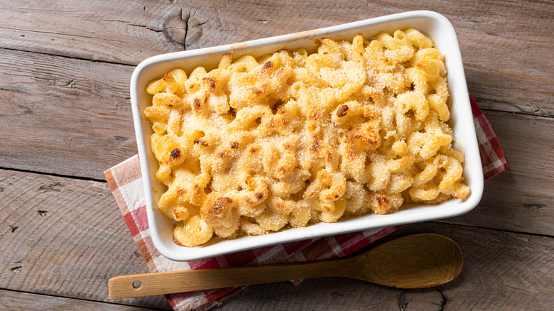 Traditional southern Mac and cheese with breadcrumbs on wooden background, top view. Homemade cheesy and creamy pasta casserole with meat.