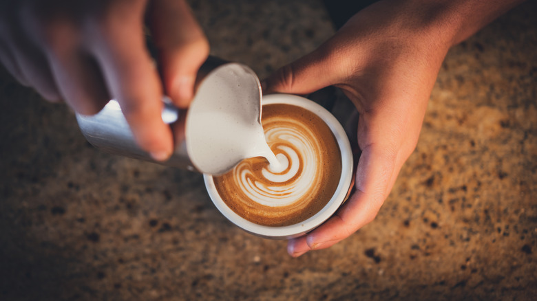 A barista pouring frothed milk into a cappuccino