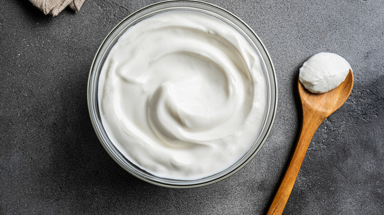 bowl of sour cream with wooden spoon beside it on black table