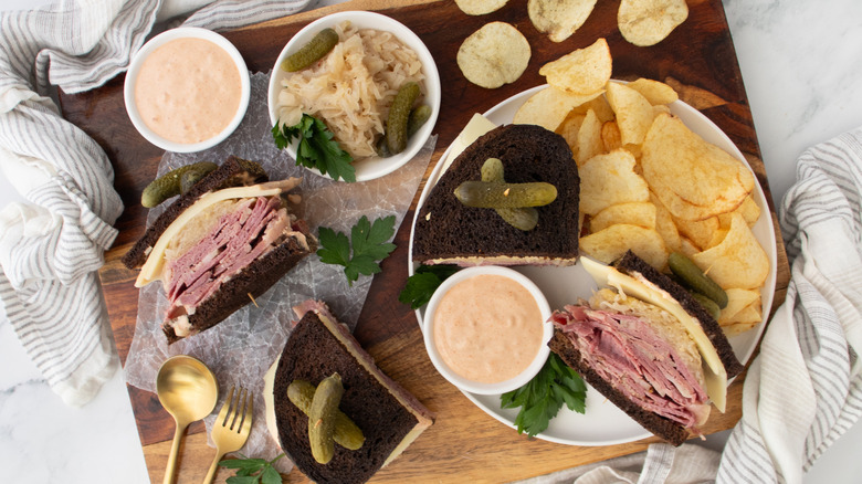 top view of sliced reuben sandwich on plate and cutting board with potato chips and dressing