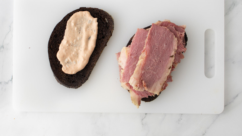 bread slices on cutting board with dressing and sliced corned beef