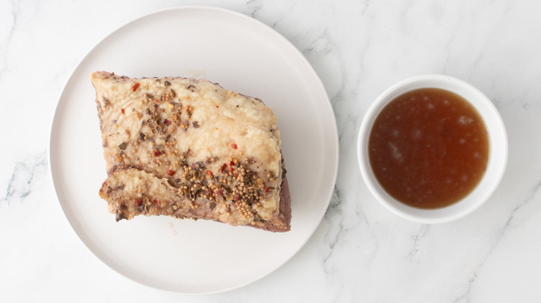 chunk of corned beef on a white plate next to a bowl of broth