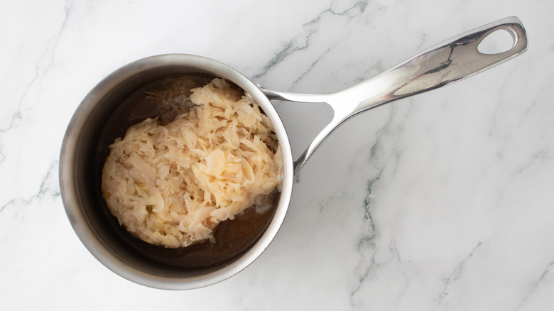 sauerkraut in saucepan with broth over marble surface