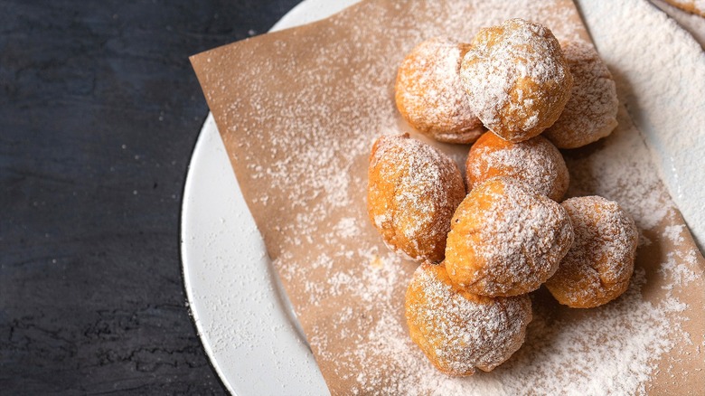 Small balls of fried dough with powdered sugar on a brown napkin over a white plate