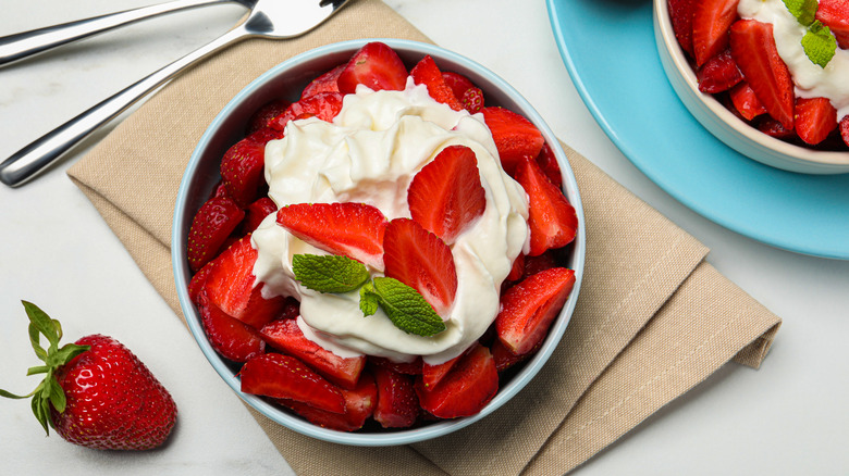 Bowl of whipped cream surrounded by strawberries.