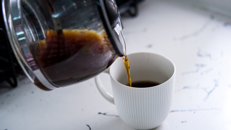person pouring pot of coffee into a cup