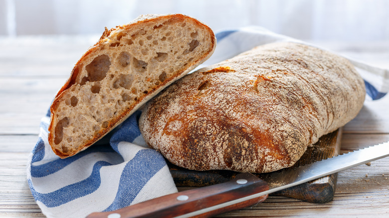 ciabatta bread loaf sliced in half on top of cloth next to knife