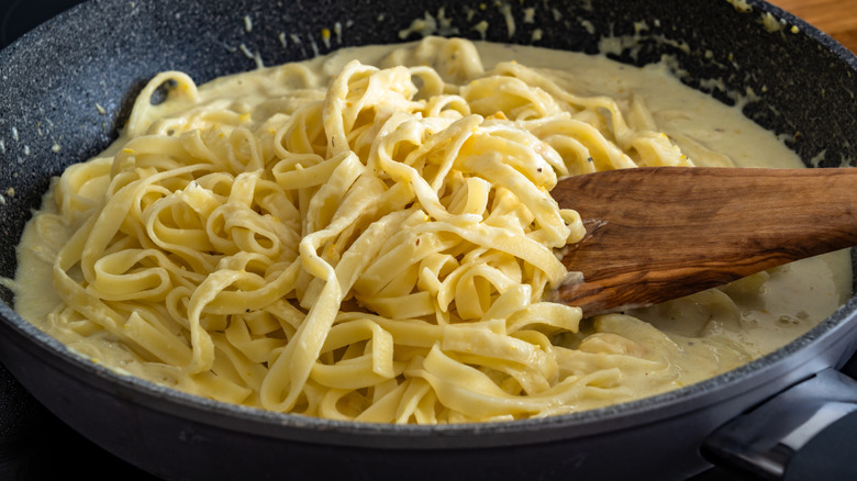 Cooking creamy chicken alfredo fettuccine pasta in frying pan