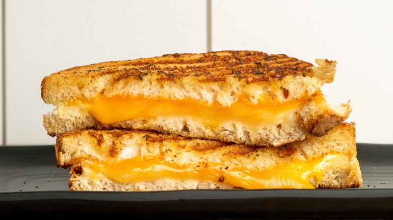 Halved grilled cheese sandwich on black board.
