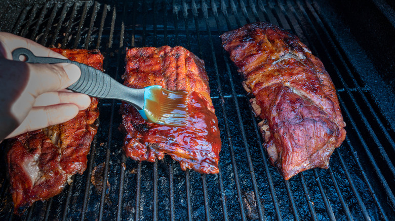 Cook basting BBQ baby back ribs with sauce.