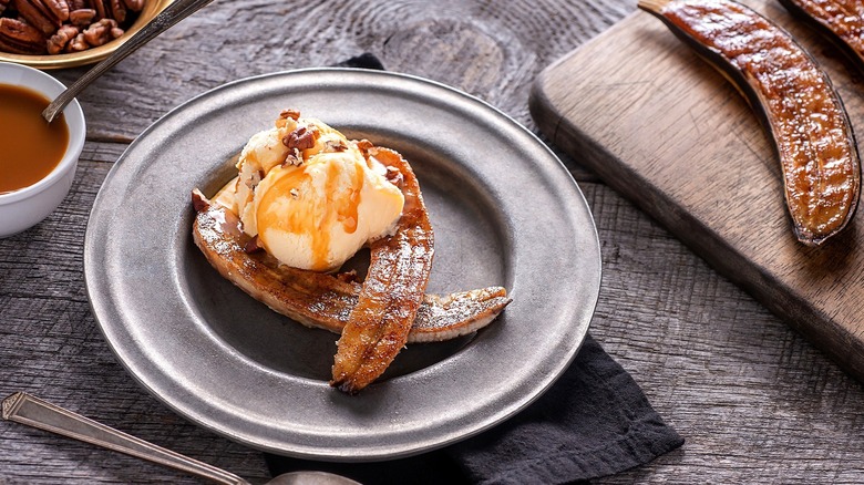 Two caramelized banana halves with vanilla ice cream and caramel sauce on a gray plate over a gray surface.