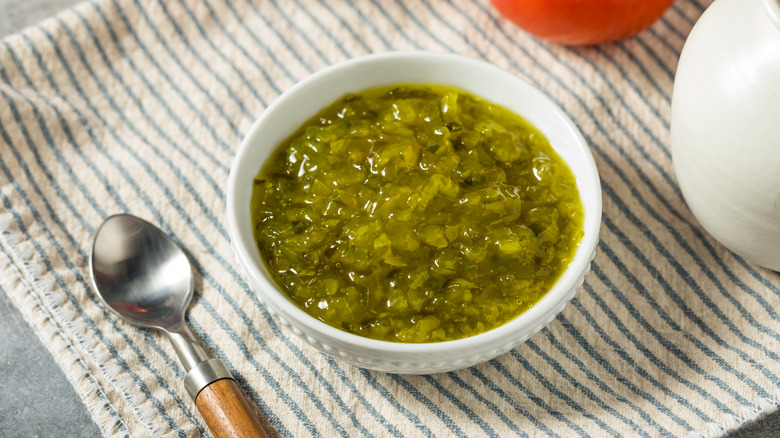 A small white bowl of green sweet relish on a blue and white striped dish towel.