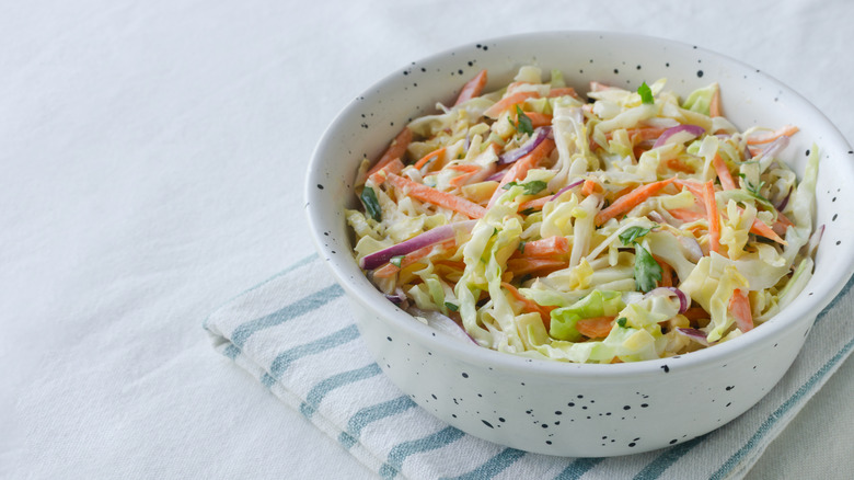 A white bowl of colorful coleslaw on a blue and white striped dish towel.