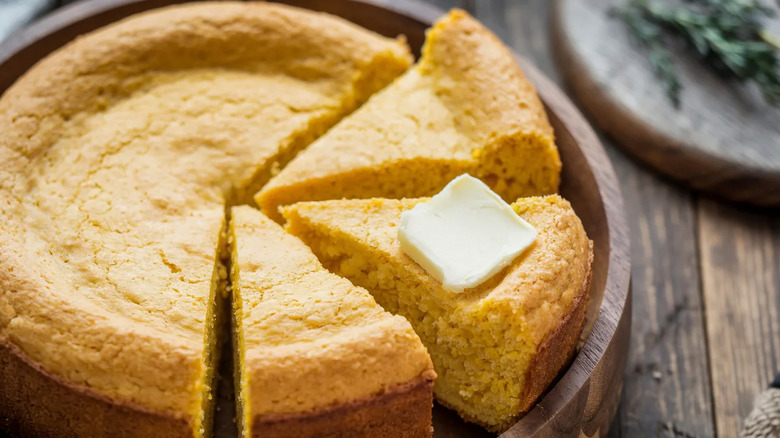 A round cornbread with three slices cut and a pat of butter on top of one slice