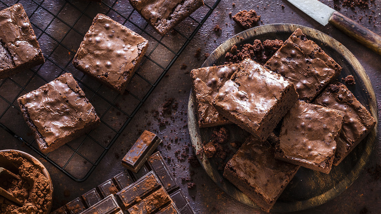 Homemade brownies are stacked on a plate and arranged on a cooling rack.