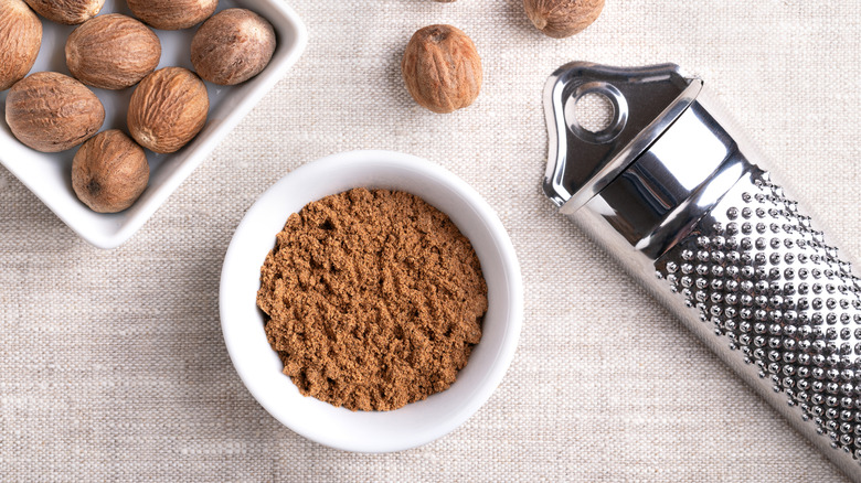 Whole nutmeg seeds are styled around a small bowl of nutmeg powder.