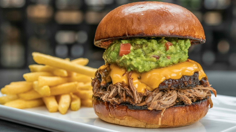 Pulled Pork Burger with Cheese and Guacamole burger, pulled pork, melted cheddar, guacamole, golden fries, casual dining, hearty meal, indulgent flavors, comfort food, food photography