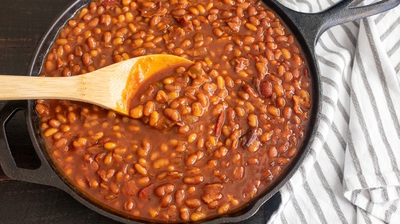 A spoon stirs baked beans in a skillet.