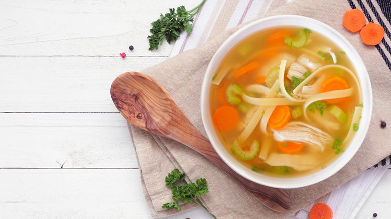Close-up of a hand opening a can of chicken noodle soup on a wooden surface