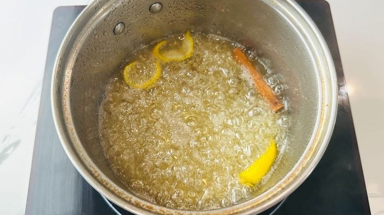 Boiling sugar water mixture with cinnamon stick and lemon peel