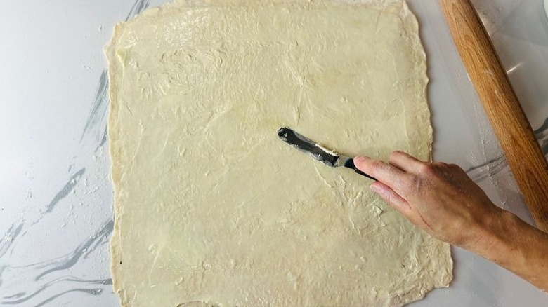 Offset spatula spreading butter onto pastry dough