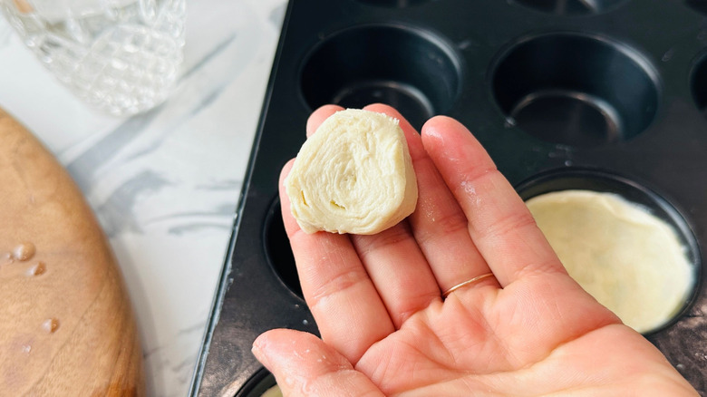 Hand holding piece of dough over muffin tin