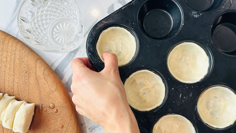 Hand pressing dough to form a cup shape inside of muffin tin